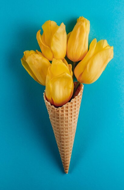 Ramo de tulipanes amarillos en cono de helado de gofre sobre un fondo azul Día de la Madre Día de San Valentín Concepto de verano Vista superior Concepto de minimalismo