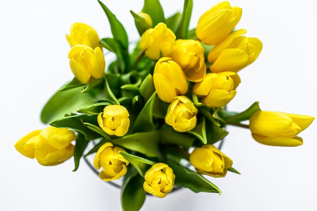 Un ramo de tulipanes amarillos en un florero de vidrio sobre un fondo blanco. La vista desde la cima. Copia espacio