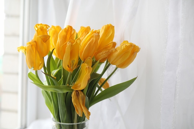Un ramo de tulipanes amarillos en un jarrón en el alféizar de la ventana. Un regalo para el día de la mujer de tulipanes amarillos. Hermosas flores amarillas en un jarrón junto a la ventana.