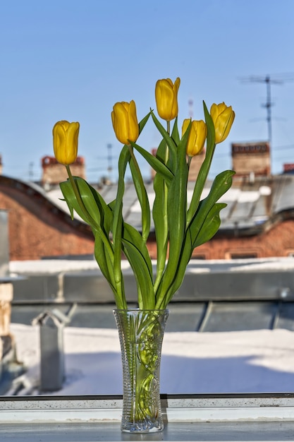 Un ramo de tulipanes amarillos en un jarrón de cristal en el alféizar de una ventana