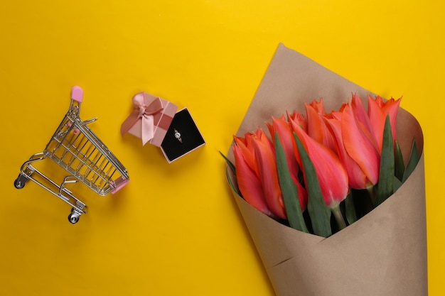 Ramo de tulipanes, anillo de oro con un diamante en una caja de regalo, carro de supermercado en amarillo