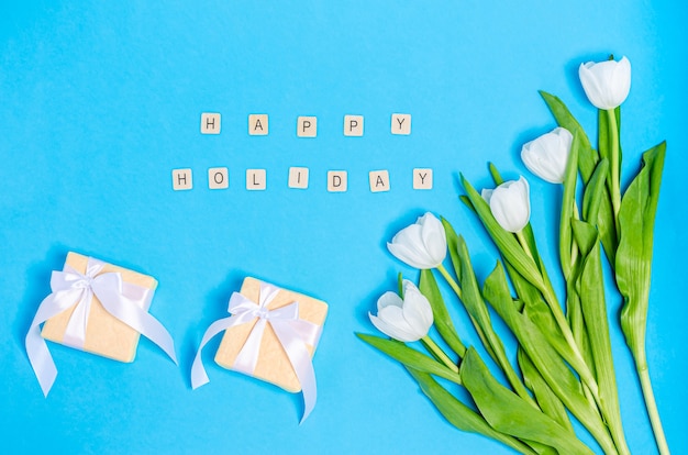 Ramo de tulipanes blancos con cajas para regalos y mesa azul de felices fiestas.