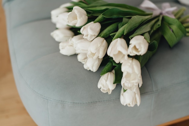 Un ramo de tulipanes blancos está acostado en una cama beige Un ramo de tulipanes está atado con una cinta lila y yace en la foto horizontal de la cama