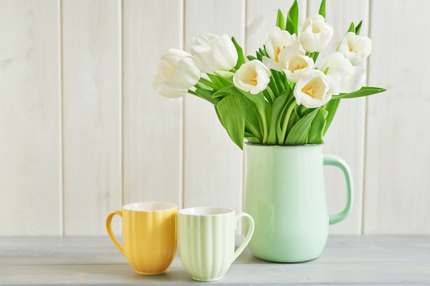 Ramo de tulipanes blancos frescos en florero y dos tazas