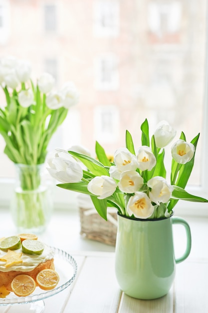 Ramo de tulipanes blancos frescos en florero y pastel con cítricos