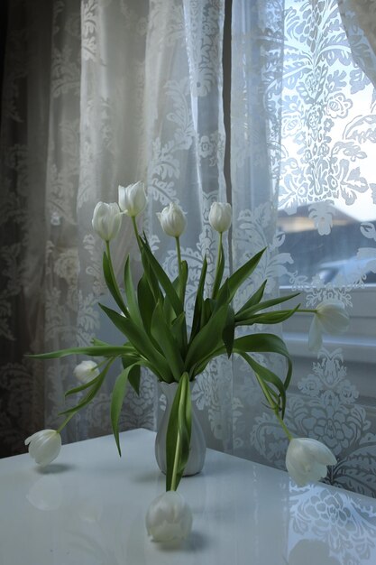 Ramo de tulipanes blancos en un jarrón sobre la mesa junto a la ventana