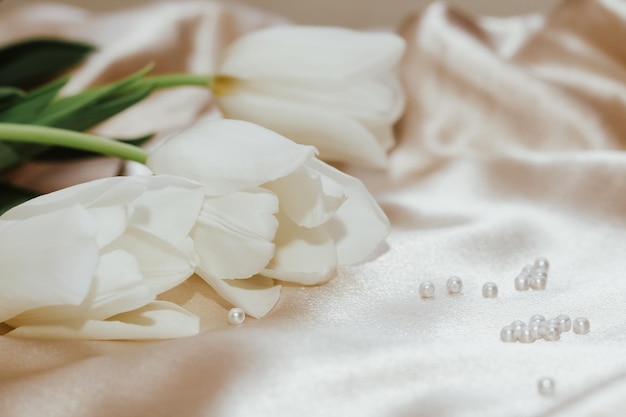 Ramo de tulipanes blancos con perlas sobre fondo satinado nude dorado seda