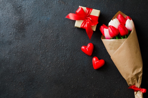 Ramo de tulipanes y caja de regalo sobre fondo oscuro.