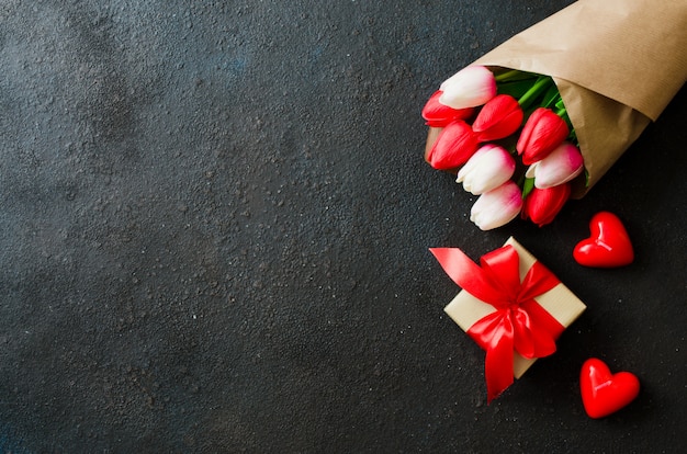 Ramo de tulipanes y caja de regalo sobre fondo oscuro.