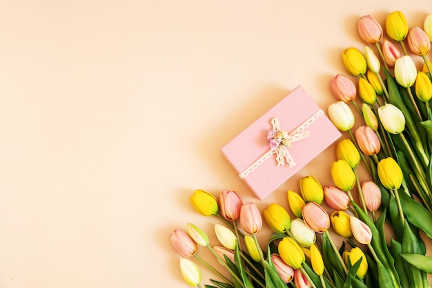 Ramo de tulipanes de colores y caja de regalo rosa aislado sobre fondo beige pastel Flores de primavera Tarjeta de felicitación para cumpleaños Mujer Día de la madre Día de San Valentín Espacio de copia plana