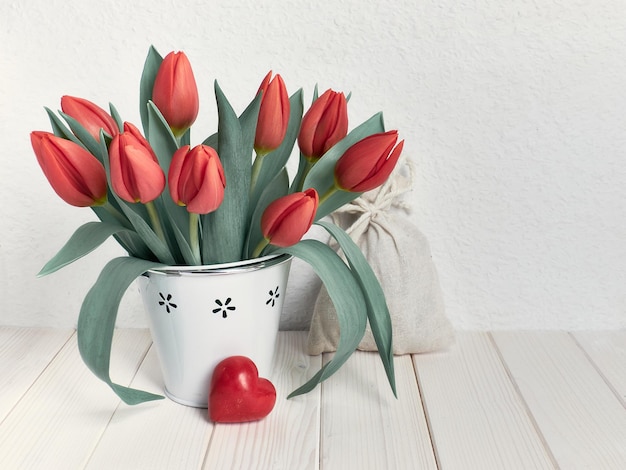 Ramo de tulipanes y corazón de piedra roja natural mesa de madera de fondo blanco.