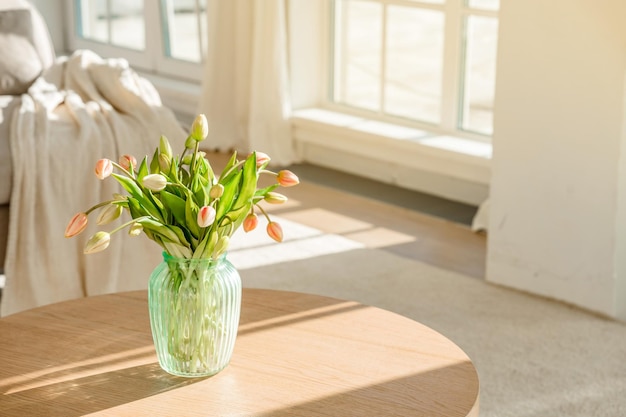 Un ramo de tulipanes en un hermoso jarrón en casa en un interior moderno y luminoso sobre una mesa de madera