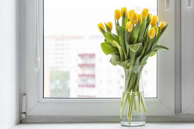 Ramo de tulipanes en jarrón de cristal en el alféizar de la ventana