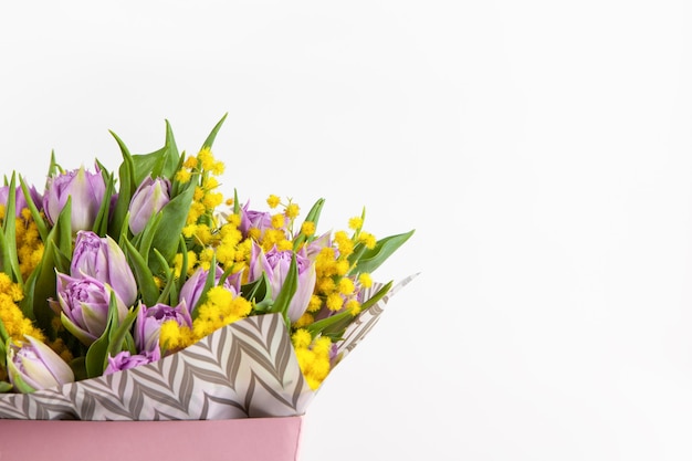 Ramo de tulipanes lilas y mimosas amarillas en caja rosa sobre blanco