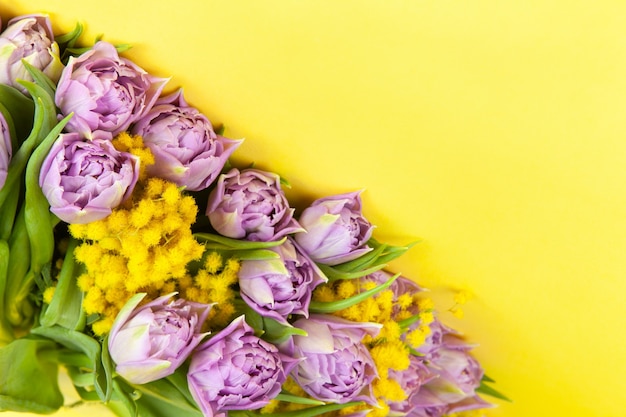 Ramo de tulipanes lilas y mimosas amarillas en pared amarilla, espacio de copia, vista superior, primer plano.