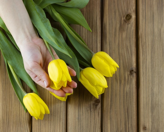 Ramo de tulipanes en una mano femenina sobre una mesa de madera