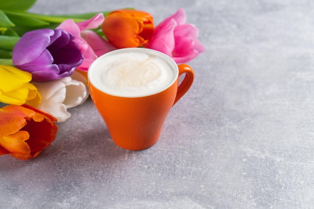 Ramo de tulipanes multicolores de primavera y taza de capuchino sobre fondo de hormigón Flores y café