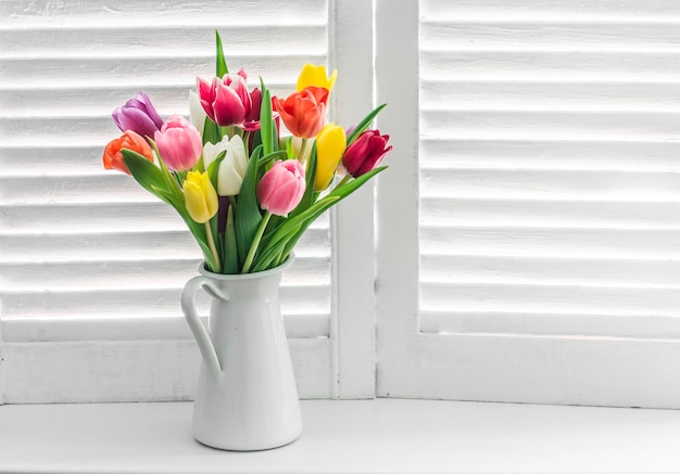 Ramo con tulipanes multicolores en una ventana con persianas de madera sobre un fondo claro