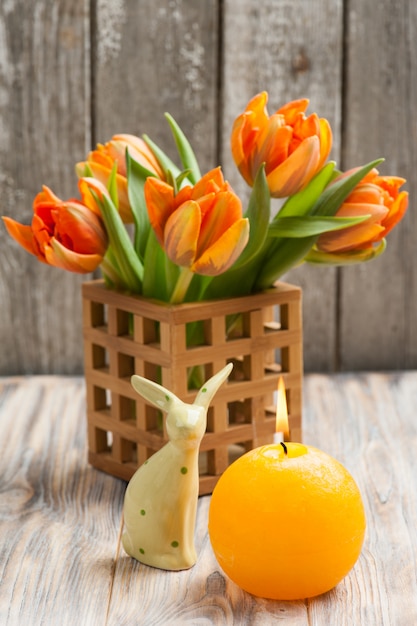 Ramo de tulipanes naranjas, velas encendidas y conejitos de pascua