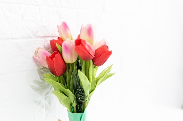 Ramo de tulipanes de primavera con flores de diferentes colores envueltos en papel para regalo sobre fondo blanco.