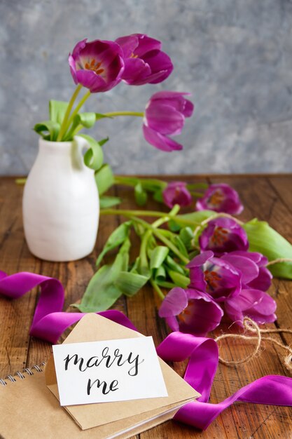 Ramo de tulipanes púrpuras y tarjeta Cásate conmigo en la mesa de madera de cerca