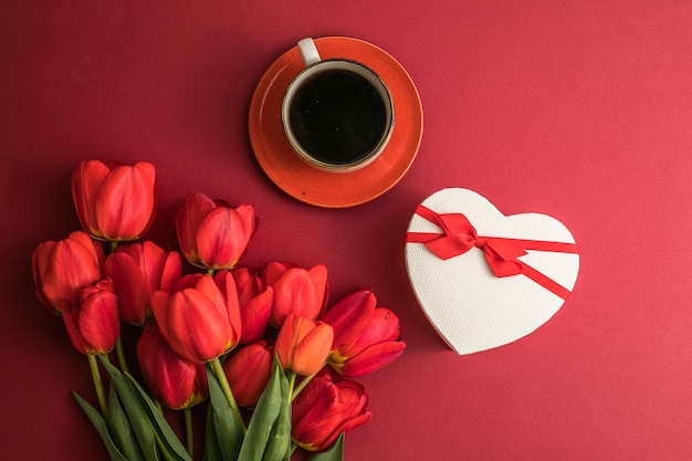 Ramo de tulipanes rojos y caja de corazón de regalo, arreglo de taza de café con mucho espacio para copiar texto