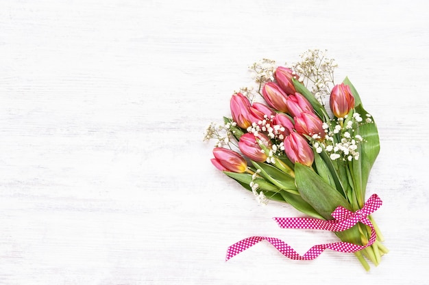 Ramo de tulipanes rosa y gypsophila decorado con cinta sobre mesa blanca. Copie el espacio, vista superior