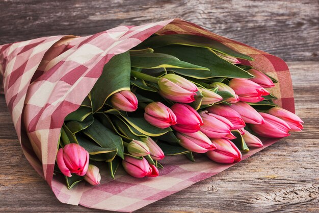 Foto ramo de tulipanes rosados envueltos en papel paquete sobre fondo de madera