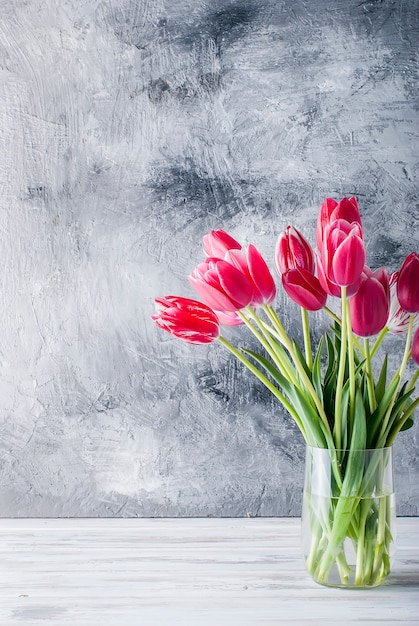 Ramo de tulipanes rosados ​​en un florero de cristal en fondo gris.