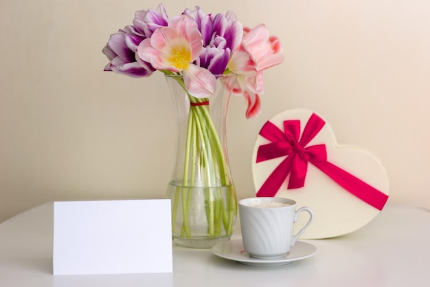 Un ramo de tulipanes rosados y morados abiertos, una caja de regalo en forma de corazón y una tarjeta vacía