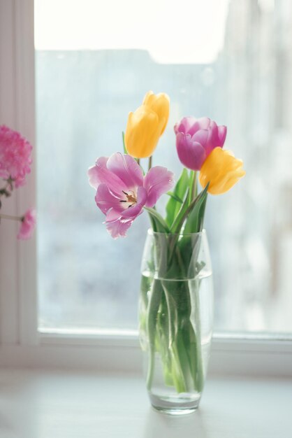 Foto ramo de tulipanes rosas y amarillos sobre fondo de luz blanca de alféizar estado de ánimo de primavera y concepto de primavera