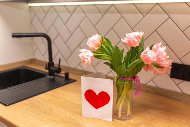 Ramo de tulipanes rosas en un jarrón de cristal con una postal en el interior blanco de la cocina