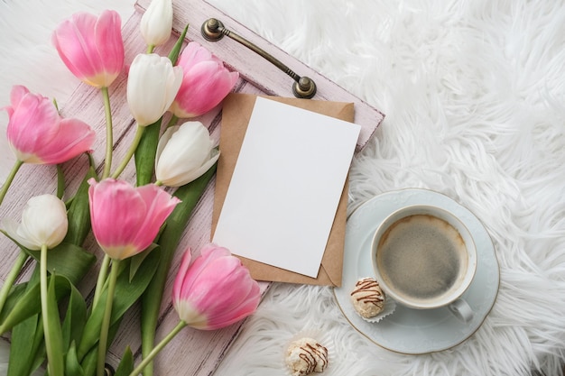Un ramo de tulipanes, una taza de café y una maqueta de una tarjeta de papel blanco en blanco para texto plano, vista superior, plac