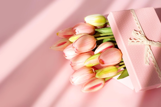 Ramo de tulipanes tiernos y caja de regalo aislada sobre fondo rosa con sombra. Flores de primavera. Tarjeta de felicitación para cumpleaños, mujer, día de la madre, boda, día de San Valentín. Endecha plana. copia espacio