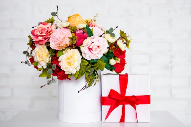 Ramo de verano de hermosas flores y caja de regalo sobre la mesa sobre fondo de pared de ladrillo blanco