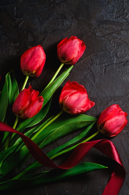 Ramo vermelho de flores tulipa com fita vermelha na mesa preta texturizada, espaço de cópia de vista superior