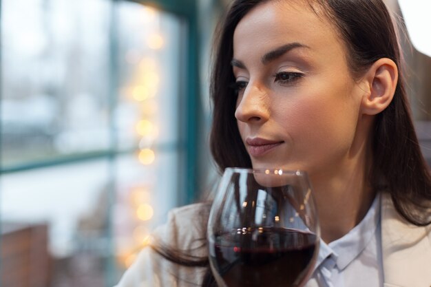 Foto ramo de vino. mujer hermosa atractiva concentrada posando con una copa de vino mientras se gira de la cámara y el pensamiento