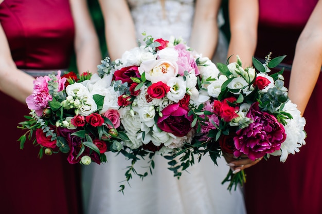 Ramos de boda en manos de la novia y las damas de honor. Peonías moradas y rosas blancas