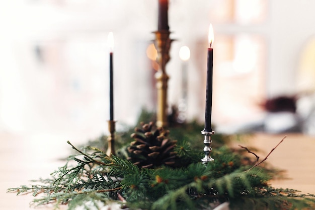 Ramos de abeto com pinhas e castiçal vintage com velas pretas acesas na mesa de madeira Arranjo rústico elegante de natal para jantar festivo Decoração de mesa rural de natal para festa