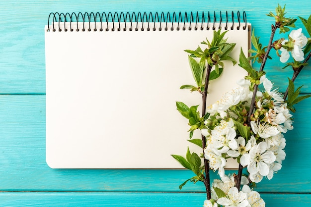 Ramos de cerejeira em flor de primavera e caderno sobre fundo azul de madeira.