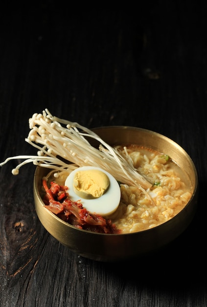 Ramyeon coreano en un tazón de oro, sirva con champiñón shimeji, kimchi y medio huevo cocido en una mesa de madera negra