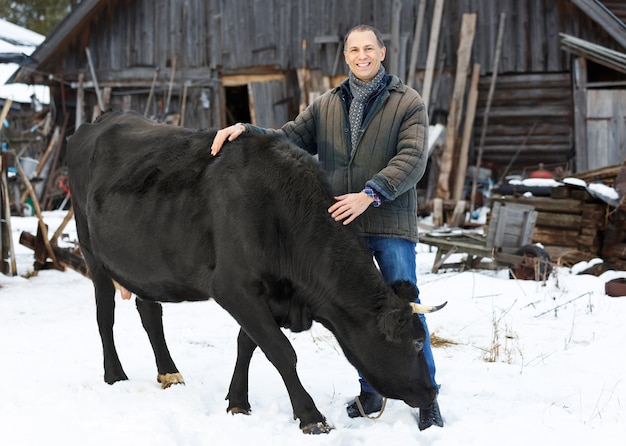 Ranchero en ropa casual de invierno se encuentra con vaca en un campo