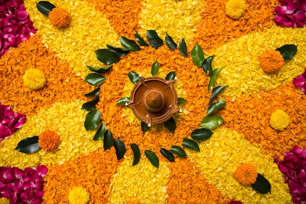 Rangoli de flores para Diwali ou Pongal feito com flores de calêndula ou zendu e pétalas de rosa vermelha sobre fundo branco com lâmpada de óleo de argila no meio, foco seletivo