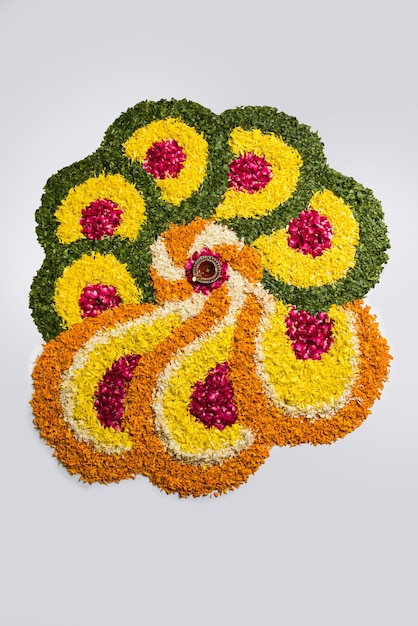 Rangoli de flores para Diwali ou Pongal feito com flores de calêndula ou zendu e pétalas de rosa vermelha sobre fundo branco com lâmpada de óleo de argila no meio, foco seletivo