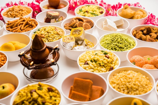 Rangoli de dulces y Farsan o bocadillos en tazones para Diwali con diya sobre fondo blanco.