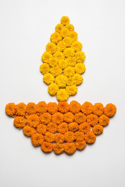 Rangoli de flores para Diwali o Pongal hecho con flores de caléndula o zendu y pétalos de rosas rojas sobre fondo blanco con lámpara de aceite de arcilla en el medio, enfoque selectivo