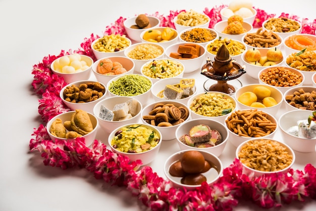 Rangoli von Süßigkeiten und Farsan oder Snacks in Schalen für Diwali mit Diya auf weißem Hintergrund