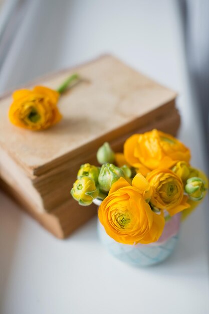 Ranunculus naranja en una linda jarra pequeña y una pila de libros antiguos en un alféizar