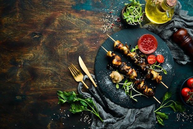 Rapana-Spieße mit Gemüse auf einer schwarzen Steinplatte Essen im Restaurant Meeresfrüchte Rustikaler Stil flach gelegt