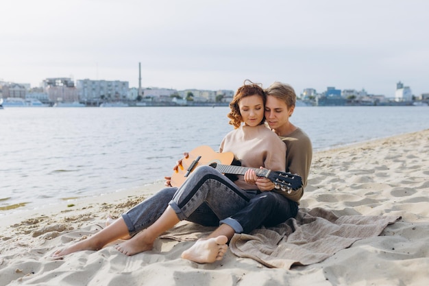 Rapariga aprendendo guitarra com professor do sexo masculino ao ar livre na praia mostrando acordes de guitarra